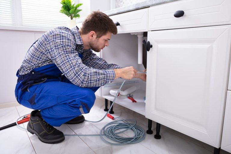 Young Male Plumber Cleaning Clogged Sink Pipe In Kitchen